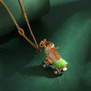 May include: Gold-tone necklace featuring a colorful roller skate pendant. The pendant is detailed with pink, green, and gold enamel, with clear rhinestone accents on the wheels. The chain is a delicate gold link.