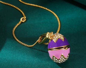 gold-tone chain necklace with a purple and pink enamel egg pendant decorated with white crystals. The pendant is a locket that can open.