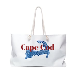 May include: White tote bag with rope handles. The bag features a blue and red graphic of the Cape Cod outline with the words "Cape Cod" in red. The bag is designed for carrying items and has a large capacity.
