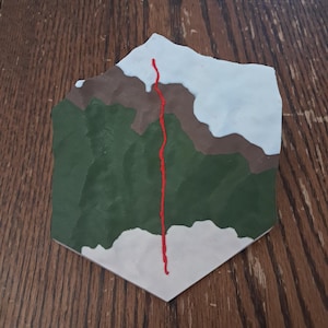 Puede incluir: Obra de arte hexagonal que representa un paisaje montañoso. La pieza presenta una base verde con detalles marrones y blancos, y una línea roja vertical. Ideal para la decoración del hogar.