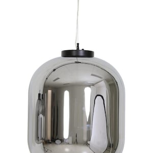 Op de afbeelding: Een moderne, reflecterende hanglamp. De lamp heeft een afgeronde, langwerpige vorm met een spiegelende, zilvergrijze afwerking. Hij hangt aan een dun, wit snoer dat aan een zwarte kap is bevestigd. Het licht reflecteert de omgeving.