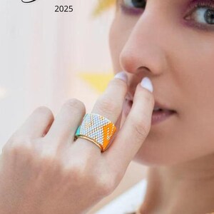May include: A colorful beaded ring with a geometric pattern in orange, turquoise, and white. The ring is gold-toned and wide, with the text "Giulia 2025" in the upper left corner.