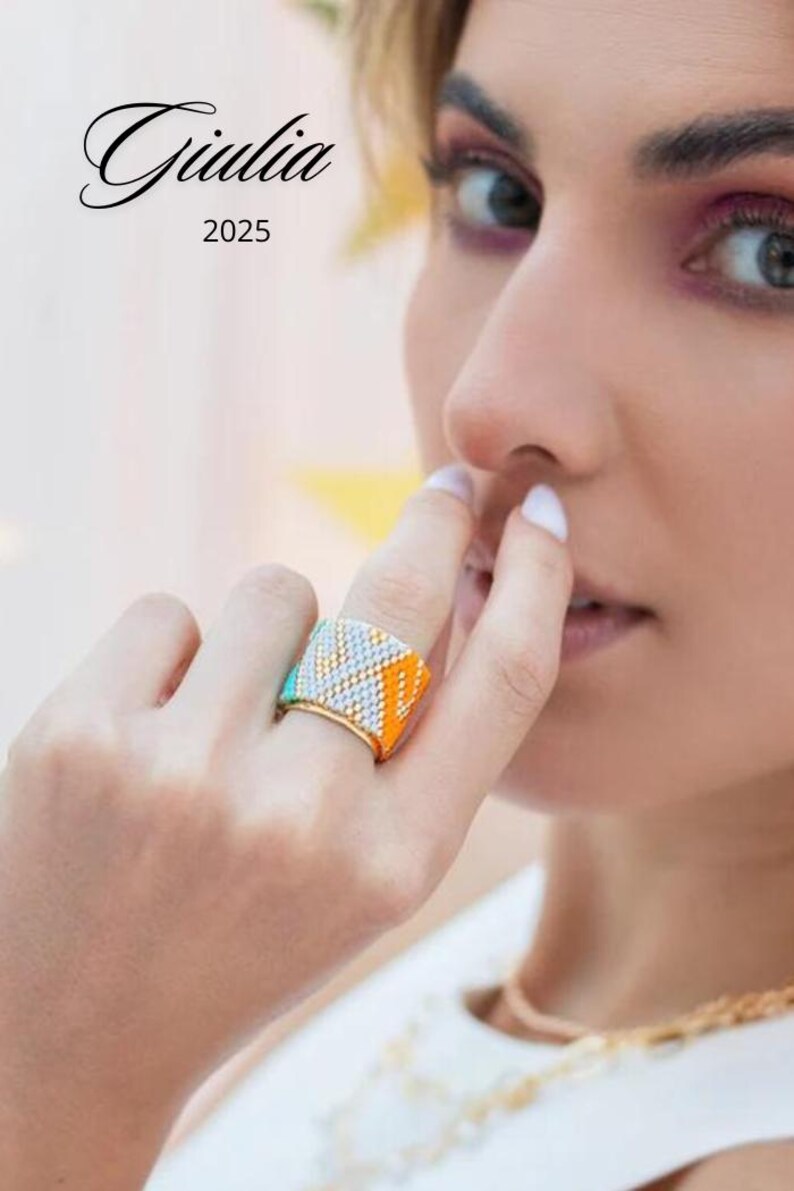 May include: A colorful beaded ring with a geometric pattern in orange, turquoise, and white. The ring is gold-toned and wide, with the text "Giulia 2025" in the upper left corner.