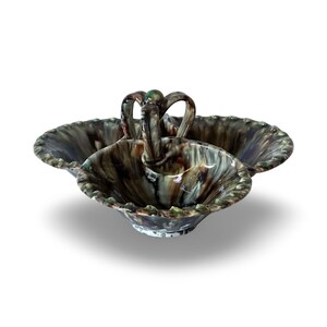 Op de afbeelding: Een keramische serveerschaal met drie secties en een centrale handgreep. De schaal heeft een gevlekte glazuur in bruin-, groen- en grijstinten. De randen hebben een decoratief, geribbeld ontwerp. De handgreep is gebogen en heeft een klein groen accent.