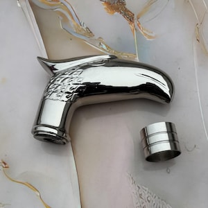 May include: A shiny silver cane handle, sculpted in the form of an eagle's head, with intricate feather detailing. A separate silver ring is also visible. The items are on a light, abstract background.
