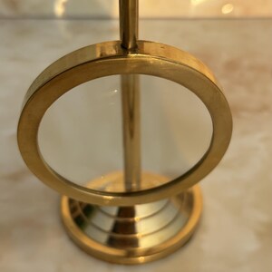 May include: A vintage-style magnifying glass with a brass finish. The round lens is held in place by a brass frame, and the base has a tiered design. The adjustable focus mechanism is visible at the top. This desk accessory is ideal for reading or detailed work.