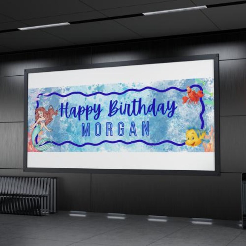 May include: A rectangular birthday banner featuring a blue watercolor background with a dark blue wavy border. The text reads Happy Birthday MORGAN in blue. Illustrations of a mermaid, a red crab, and a yellow fish are positioned on the banner.