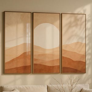 Peut inclure: Trois tableaux abstraits encadrés représentant un paysage désertique aux tons terreux de brun et beige. La pièce centrale présente un grand cercle blanc cassé ressemblant au soleil. L'œuvre est au-dessus d'un canapé beige.