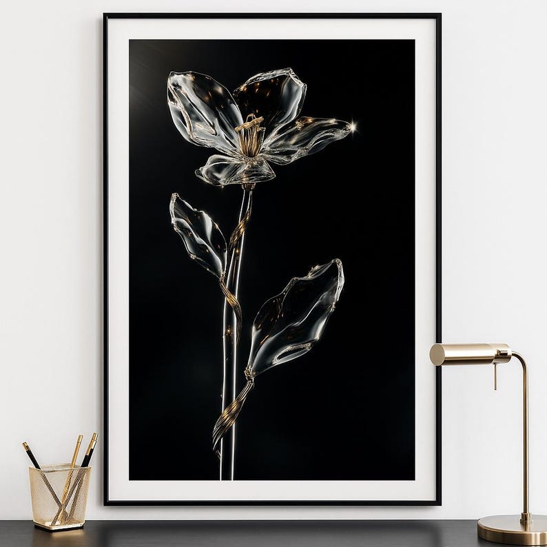 May include: A clear glass flower with a gold stem and accents, set against a black background. The flower has delicate petals and leaves, creating a striking contrast. The artwork is framed in a black frame.