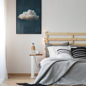 Könnte beinhalten: Schlafzimmer-Interieur mit einem gerahmten Wolkenkunstdruck über einem Bett mit grauer Bettwäsche und dekorativen Kissen. Ein kleiner Beistelltisch mit einer Lampe und einer weißen Schale. Ein schwarz-weiß gemusterter Teppich liegt auf dem Holzboden.