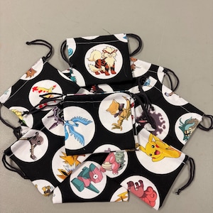 Puede incluir: Bolsas negras con cordón con círculos blancos con varios personajes de dibujos animados. Las bolsas tienen cordones negros. Los personajes son de diferentes colores, incluyendo rojo, amarillo, azul y verde.