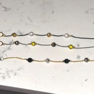 May include: Three bracelets featuring delicate metal chains with alternating spherical beads. The top bracelet has dark chains with gold and silver textured beads. The middle has silver chains with yellow and dark beads. The bottom has gold chains with black and silver beads.