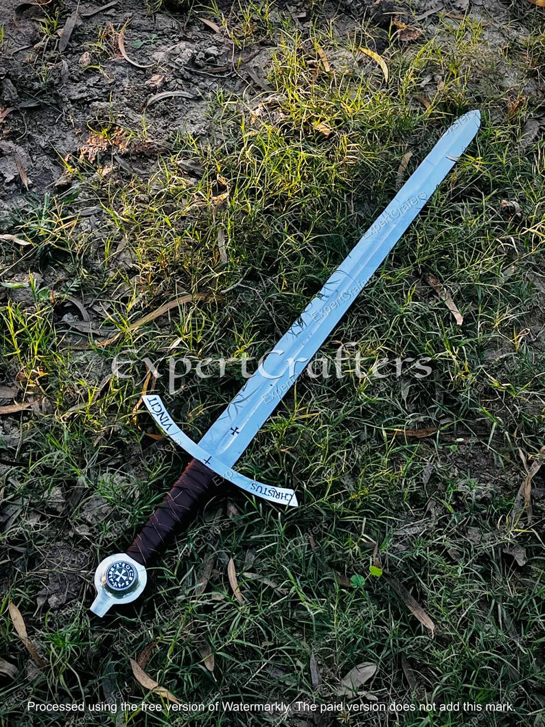 May include: A silver sword with a brown leather-wrapped handle and a cross-shaped guard. The blade has etched designs and the words "VINCIT" and "CHRISTUS". The sword rests on a bed of grass and dirt.