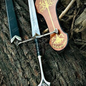 May include: A silver and black sword with a leather-wrapped handle and a decorative hilt. The blade is etched with text. A brown shield with a gold tree design is also present. The items are displayed on a textured, brown surface.