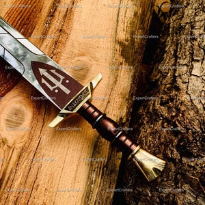 May include: A detailed view of a decorative sword with a brown handle and a silver blade. The sword features gold accents and a brown emblem with a trident symbol. The handle has a textured design, and the blade is partially visible.