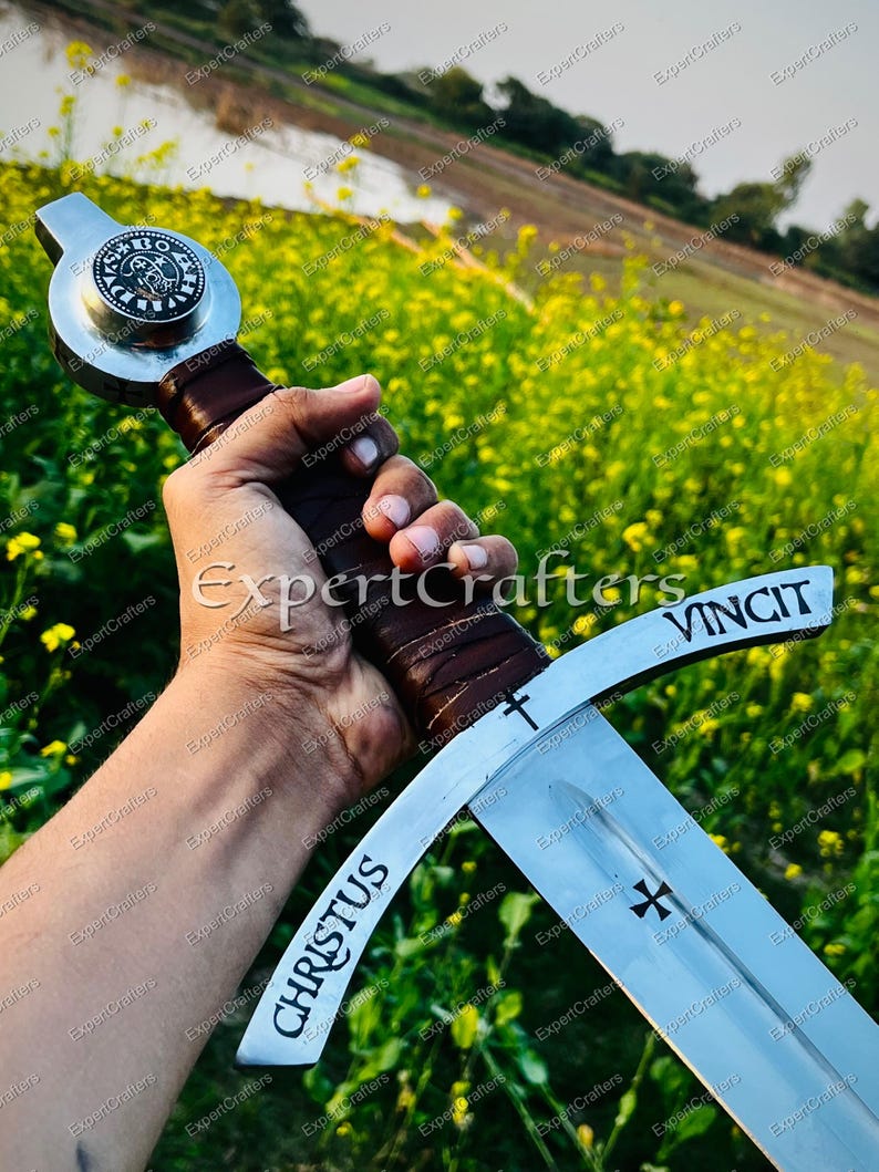 May include: A medieval sword with a silver blade and a brown leather-wrapped handle. The blade features the words "CHRISTUS" and "VINCIT", along with a cross symbol. The sword's hilt has a circular emblem.
