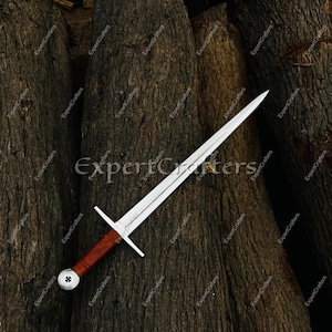 May include: A medieval sword with a silver blade and a brown leather-wrapped handle. The sword features a crossguard and a decorative pommel. The image is set against a backdrop of dark, textured wood.