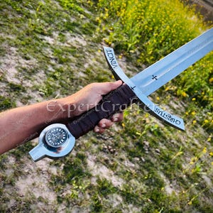 May include: A medieval-style sword with a silver blade and a brown leather-wrapped handle. The crossguard features the word "CHRISTUS" and a cross symbol. The pommel has a circular design. The word "VINCIT" is inscribed on the blade.