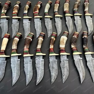 Peut inclure: Une collection de couteaux de chasse avec des lames à motifs et des manches décoratifs. Les manches présentent une variété de couleurs et de textures, avec un étui en cuir visible à droite. Les lames ont un design gravé unique.