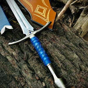 May include: A silver and blue sword with a decorative hilt and a blue handle. The sword is displayed with a brown shield with gold accents. The sword's blade is approximately 24 inches long.