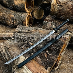 Könnte beinhalten: Ein japanisches Katana-Schwert mit schwarzem Griff und Scheide, das auf einer Holzoberfläche liegt. Die silberne Klinge hat geätzte Muster. Der Hintergrund zeigt gestapelte Baumstämme.
