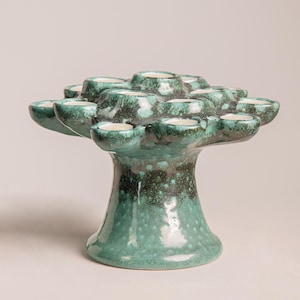 May include: A teal ceramic candle holder with multiple small cup-shaped holders. The candle holder has a tree-like design with a wide base and a textured, speckled finish. The teal colour transitions to a darker green near the base.