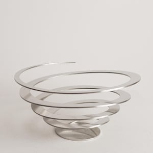 Può includere: Una moderna ciotola decorativa color argento con un design a spirale. La ciotola è in metallo e presenta una serie di anelli concentrici che creano un effetto vorticoso. Poggia su una piccola base circolare.