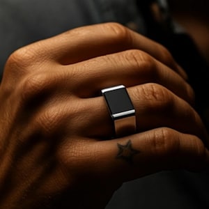 May include: A silver ring with a rectangular black onyx stone. The ring is shown on a hand with a star tattoo. The ring has a modern, minimalist design. The brand logo "PIKOSAL" is in the bottom right corner.