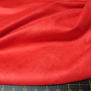 May include: A close-up of a bright red fabric with a soft, fuzzy texture. The fabric is folded and draped, showing its smooth surface and subtle sheen.