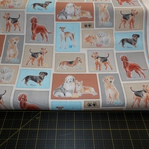 Op de afbeelding: Witte stof met een herhaald patroon van verschillende hondenrassen in rechthoekige kaders. De honden zijn afgebeeld in een aquarel stijl, met diverse kleuren en poses. Sommige kaders bevatten hondenbakken en pootafdrukken.