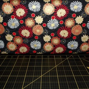 May include: Black fabric with a repeating pattern of red, white and gold flowers. The fabric has a subtle shimmer.