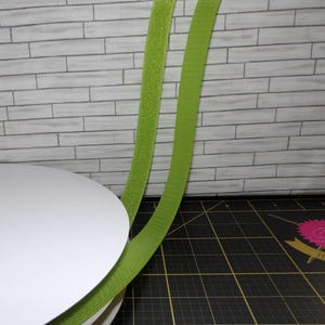 May include: Two strips of lime green hook and loop fastener tape. The tape is shown against a white brick wall and a black cutting mat.