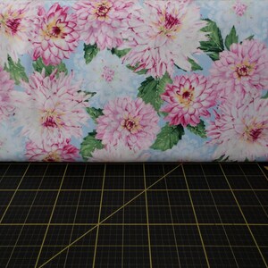 May include: A light blue fabric with a pink floral pattern. The flowers are large and have a watercolour effect. The fabric is ideal for quilting, crafts, and home decor.