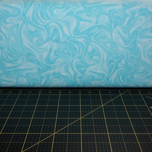 May include: A close-up of a light blue fabric with a white marbled pattern. The fabric is lying on a black cutting mat with a ruler and a sewing needle.