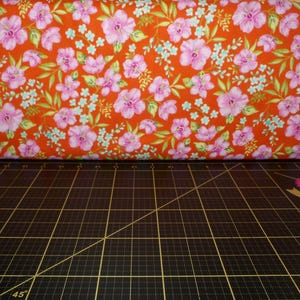 May include: Red fabric with a pink floral pattern. The fabric is on a black cutting mat.