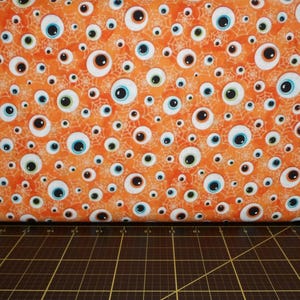 May include: Orange fabric with a repeating pattern of white eyeballs with blue and green irises and white spiderwebs.
