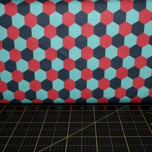 Puede incluir: Una tela con un patr&oacute;n repetido de hex&aacute;gonos rojos, azules y negros. La tela tiene una textura sutil.
