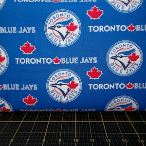 May include: Blue and white fabric with a repeating pattern of the Toronto Blue Jays logo, the words "Toronto Blue Jays", and a red maple leaf.