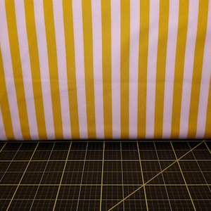 Może przedstawiać: Tkanina w żółto-białe pasy z czarno-żółtym wzorem kratki pod spodem.
