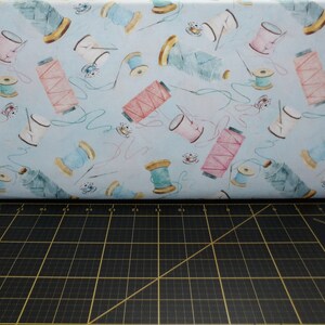 May include: A blue and white fabric with a repeating pattern of spools of thread, needles, and other sewing supplies. The fabric is on a black cutting mat.