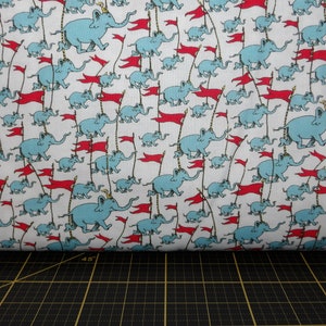 May include: White fabric with a repeating pattern of blue elephants carrying red flags. The elephants are marching in a line.