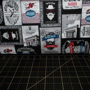 May include: Black and white fabric with a repeating pattern of barber shop themed illustrations. The illustrations include scissors, razors, barber poles, and text that says "Barber Shop", "Quality", "Daily Special", and "Hipster".