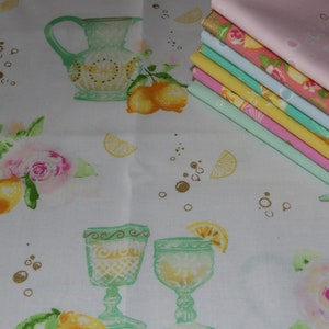 Könnte beinhalten: Ein Stapel von acht Stoffquadraten mit einem Zitronen- und Blumenmuster. Der Stoff ist weiß mit gelben Zitronen, rosa Rosen und grünen Blättern. Der Stoff ist mit goldenem Glitzer verziert. Die Stoffquadrate sind übereinander gestapelt, wobei das oberste Quadrat rosa und das unterste Quadrat grün ist.