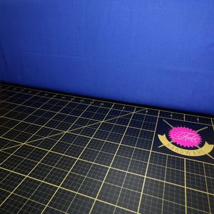 May include: A black cutting mat with a grid pattern and gold lines. The mat has a pink and gold logo that says "Tula Pink Hardware".