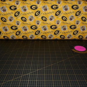 Puede incluir: Una tela amarilla con un patrón repetido de cabezas de tigre negras y las palabras "GRAMBLING STATE UNIVERSITY" en un óvalo negro.