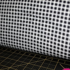 May include: Black and white gingham fabric with a small check pattern. The fabric is rolled up and sitting on a black cutting mat.