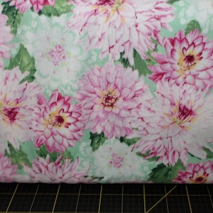 May include: A close-up of a fabric with a floral pattern. The fabric features pink and white flowers with green leaves on a light green background.