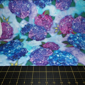 May include: A blue and purple floral fabric with a watercolor background. The fabric features a repeating pattern of hydrangeas in shades of blue, purple, and pink.