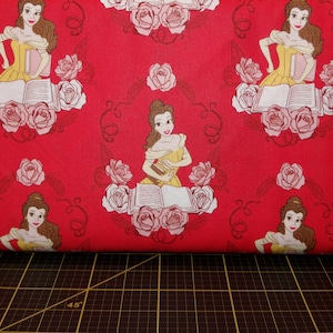 May include: Red fabric with a repeating pattern of Belle from Beauty and the Beast. Belle is depicted holding a book and surrounded by roses.