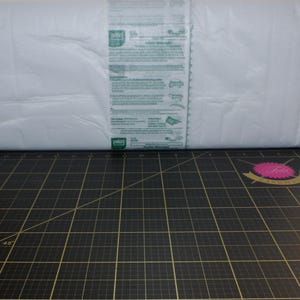 May include: A white package of Pellon fusible interfacing. The package is on a black cutting mat with a pink and gold logo.